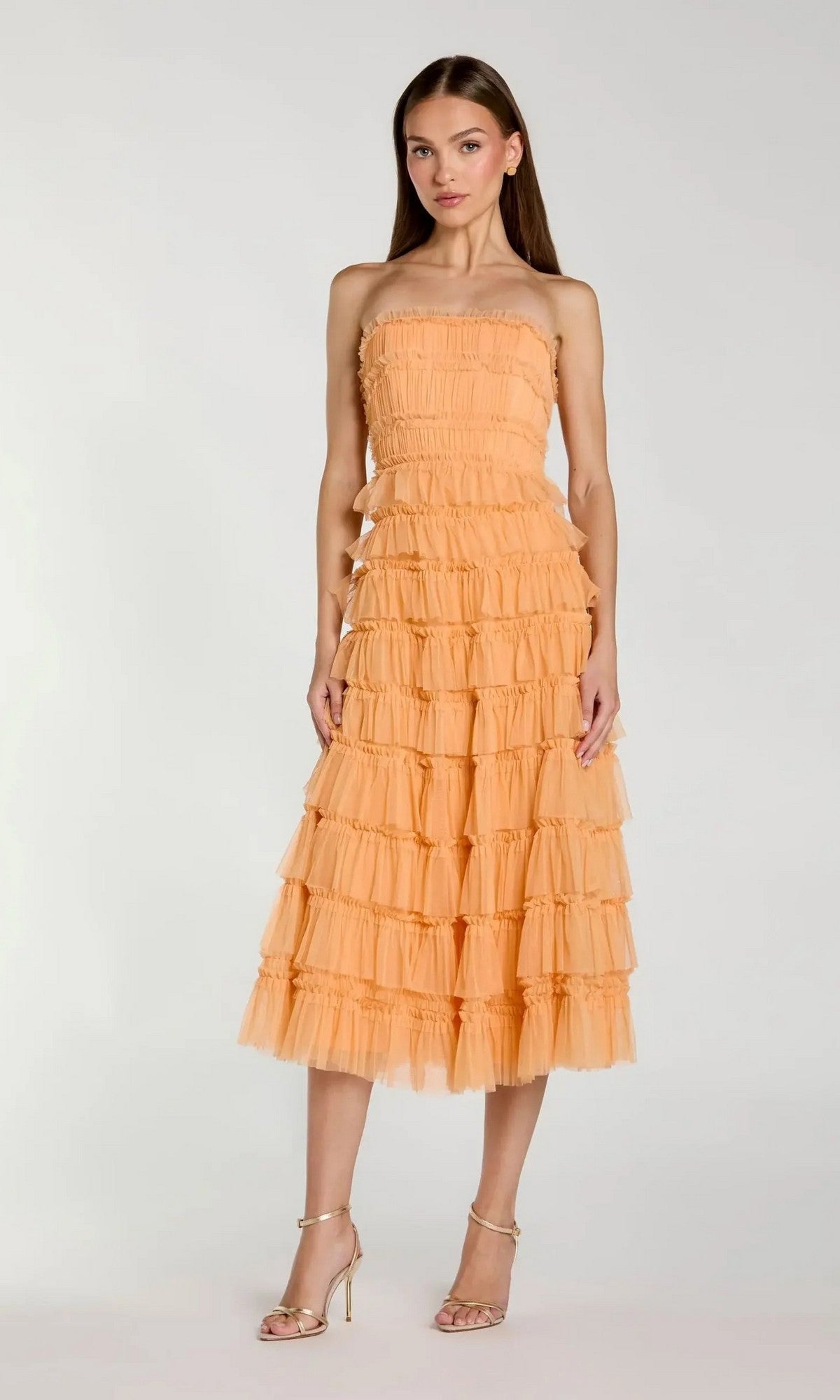 A woman stands against a plain light background wearing the Mac Duggal 8286 Midi Semi-Formal Dress, featuring peach micro-ruffle detailing and strappy high-heeled sandals.